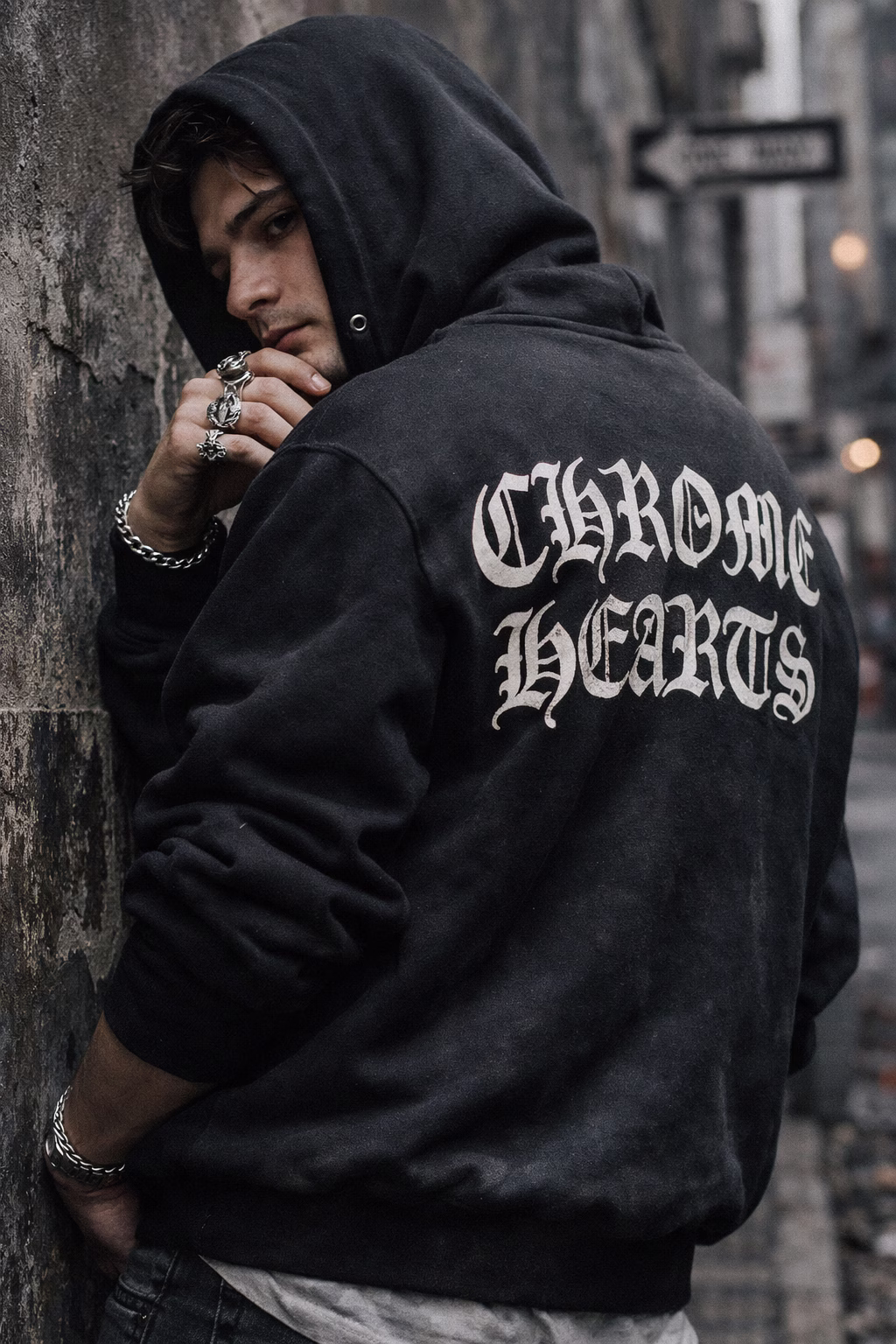 Young man wearing a Chrome Hearts hoodie and silver rings in an urban street, showcasing luxury streetwear style